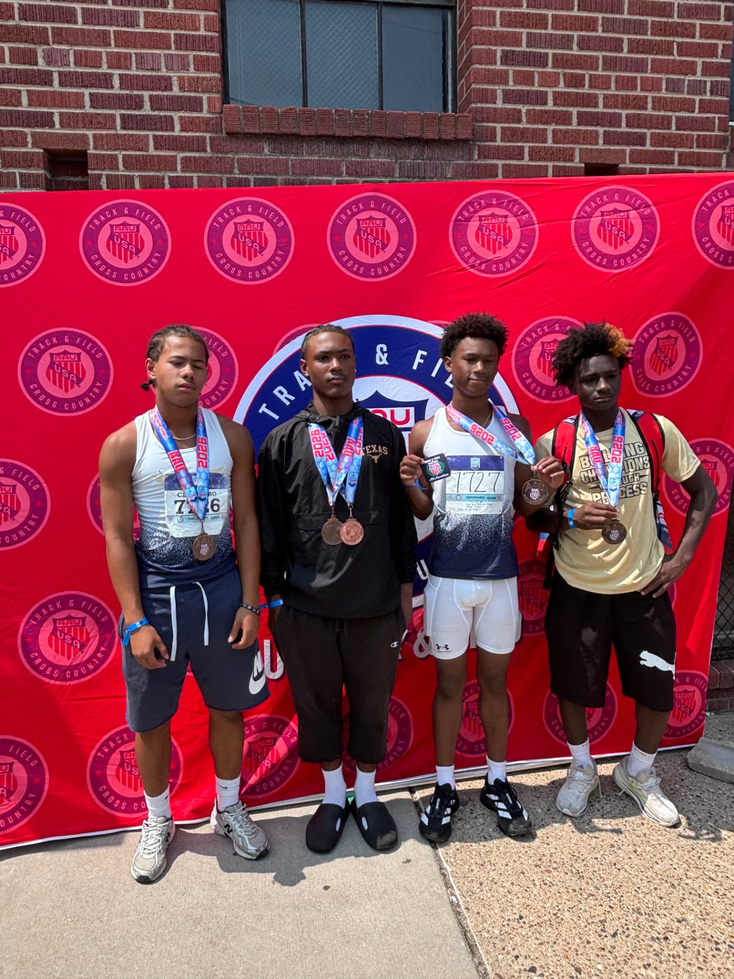 Four TSE athletes with medals at the AAU Junior Olympic Games backdrop
